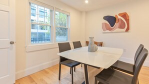 A dining area with a white table, black chairs, a vase, and a painting on the wall.