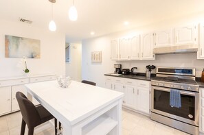 A modern kitchen with white cabinets, stainless steel appliances, and pendant lighting.
