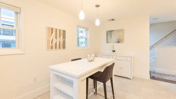 A modern kitchen with a white countertop, two pendant lights, and a dining area with a white table and chairs.