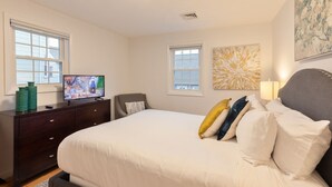 A bedroom with a bed, a television on a dresser, and two windows.