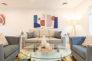 Ein modernes Wohnzimmer mit einer Sofagarnitur, einem Glastisch und abstrakter Wandkunst.