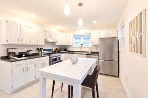 A modern kitchen with white cabinets, stainless steel appliances, and a central island with chairs. - Private Home Near Kendall Sq (Cambridge)
