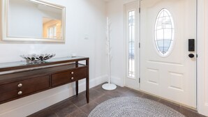 A clean, white interior with a wooden console table, a large mirror, and a door with a frosted glass window.