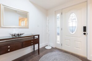 A clean, white entryway with a wooden console table, a large mirror, and a white door with a glass panel. - Private Home Near Kendall Sq (Cambridge)