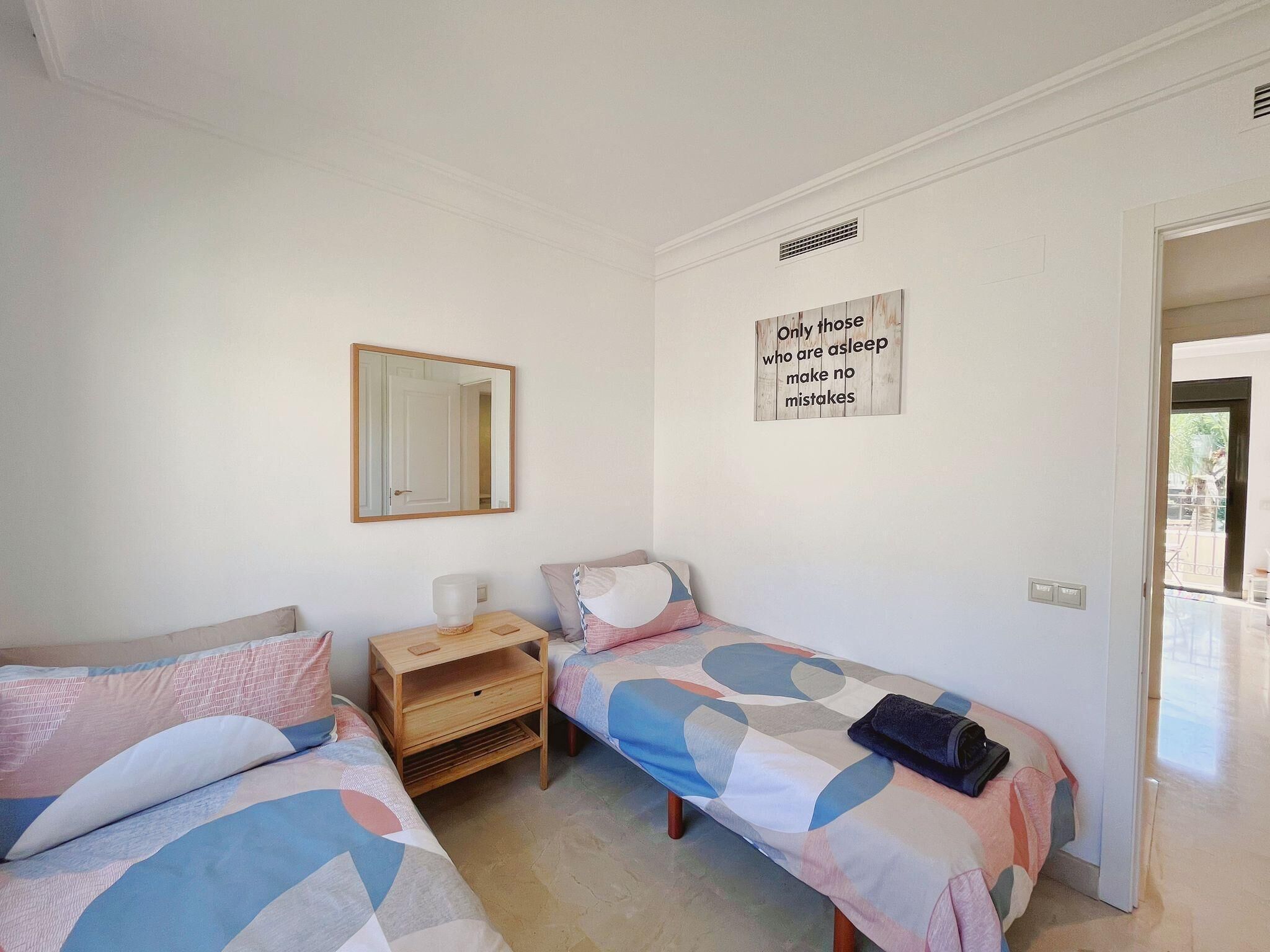 A bedroom with two beds, a bedside table, a mirror, and a motivational quote on the wall.