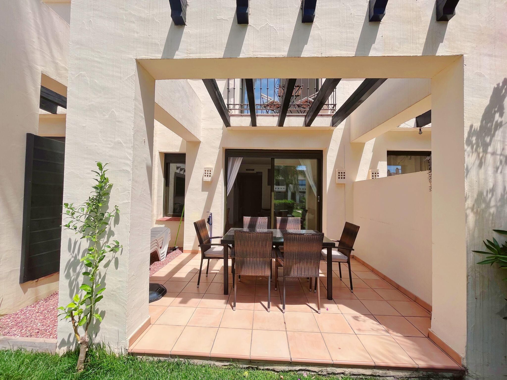 Un patio cubierto con mesa y sillas, una planta pequeña y vistas al exterior.