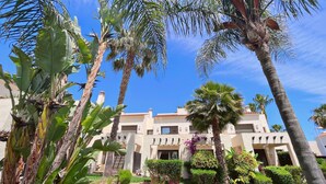 A resort with palm trees, a well-maintained lawn, and a building with a tiled roof. - Casa Mila Roda Sleeps 4 With Pool (San Javier)