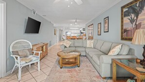 Ein Wohnzimmer mit einer Couch, Sesseln, einem Couchtisch, einem Fernseher und einem Deckenventilator.