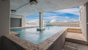 Ein Pool auf dem Dach mit klarem, blauem Wasser, einer Beton Decke und Blick auf eine Stadtlandschaft mit Palmen.
