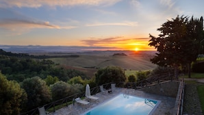 A pool with lounge chairs and a stone deck, surrounded by greenery and a scenic view of hills and a sunset. - Villa Frantusina Volterra (Volterra)
