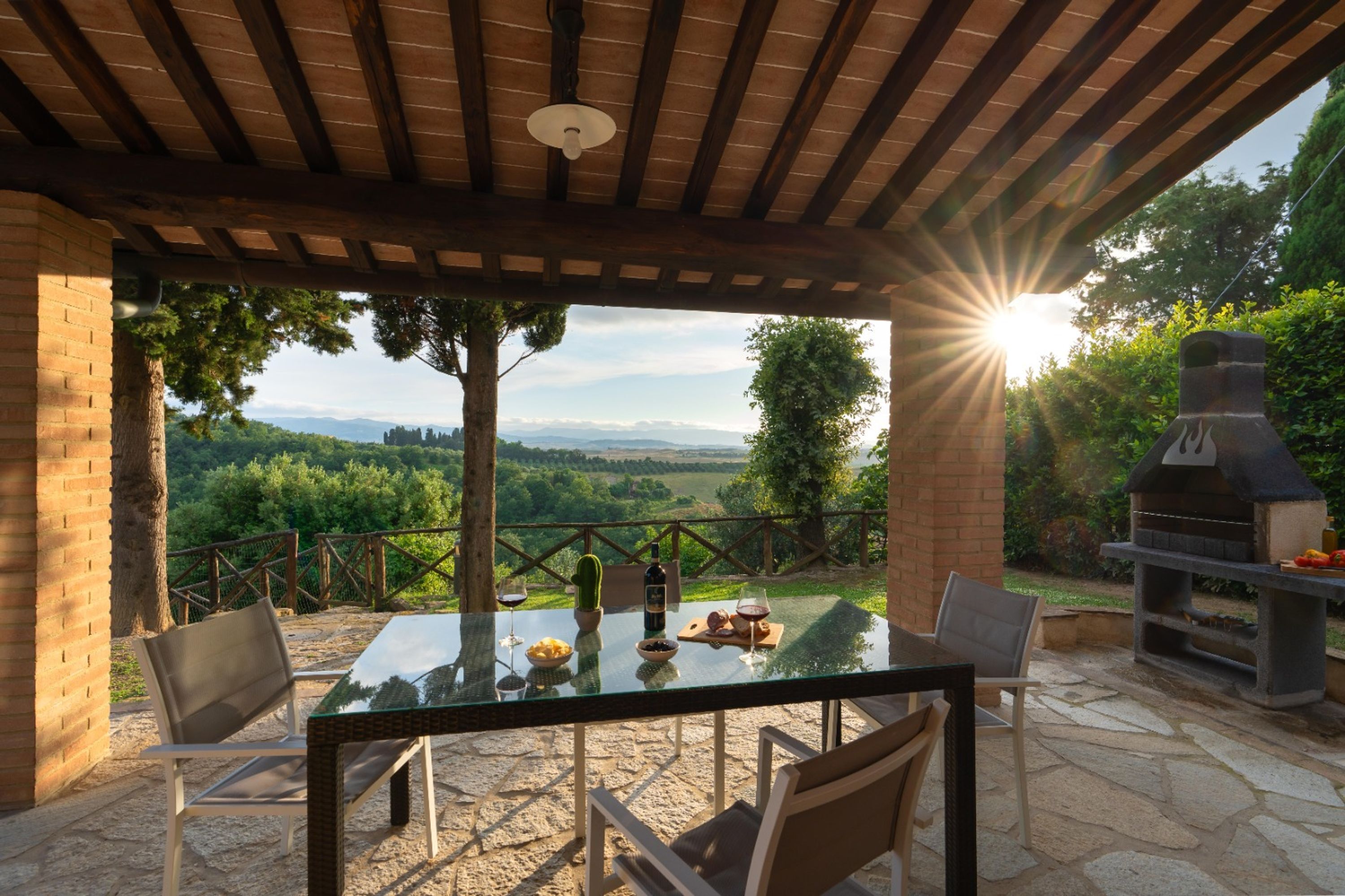 An outdoor patio with a glass table, chairs, and a brick barbecue grill.