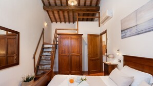 A bedroom with a wooden staircase, a bed with white bedding, a small table with a glass of orange juice, and a painting on the wall. - Villa Frantusina Volterra (Volterra)