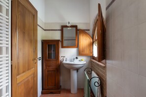 A bathroom with a wooden door, a sink, a mirror, and a towel rack. - Villa Frantusina Volterra (Volterra)