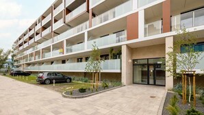 Un edificio residencial de varios pisos con balcones, una zona de estacionamiento y jardines ajardinados.