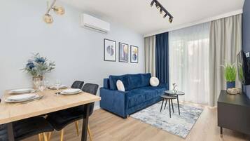 Ein modernes Wohnzimmer mit einem blauen Sofa, einem Esstisch für vier Personen und einem Fernseher auf einem Beistelltisch.