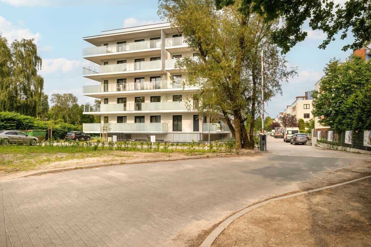 Un edificio residencial de varios pisos con balcones, un camino de entrada pavimentado y automóviles estacionados.