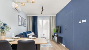 Una sala de estar moderna con comedor, un sofá, un televisor y un amplio ventanal con cortinas.