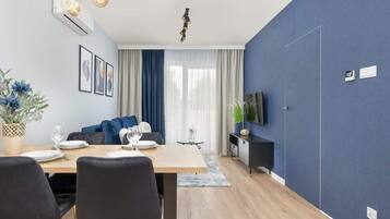 Un salon moderne comprenant un coin repas, un canapé, un téléviseur et une grande fenêtre avec des rideaux.