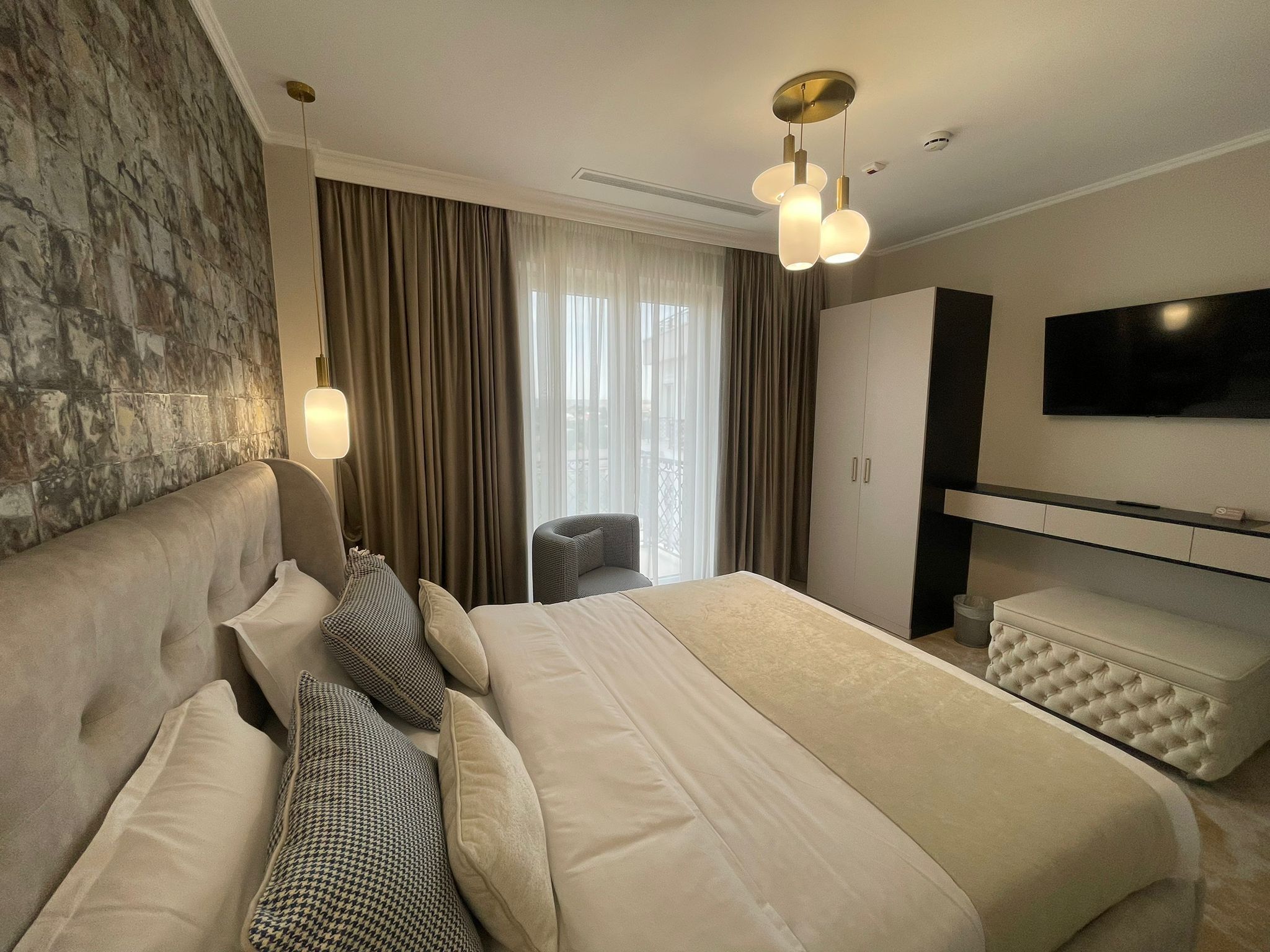 A modern hotel room with a large bed, a sofa, a TV, and a wardrobe.
