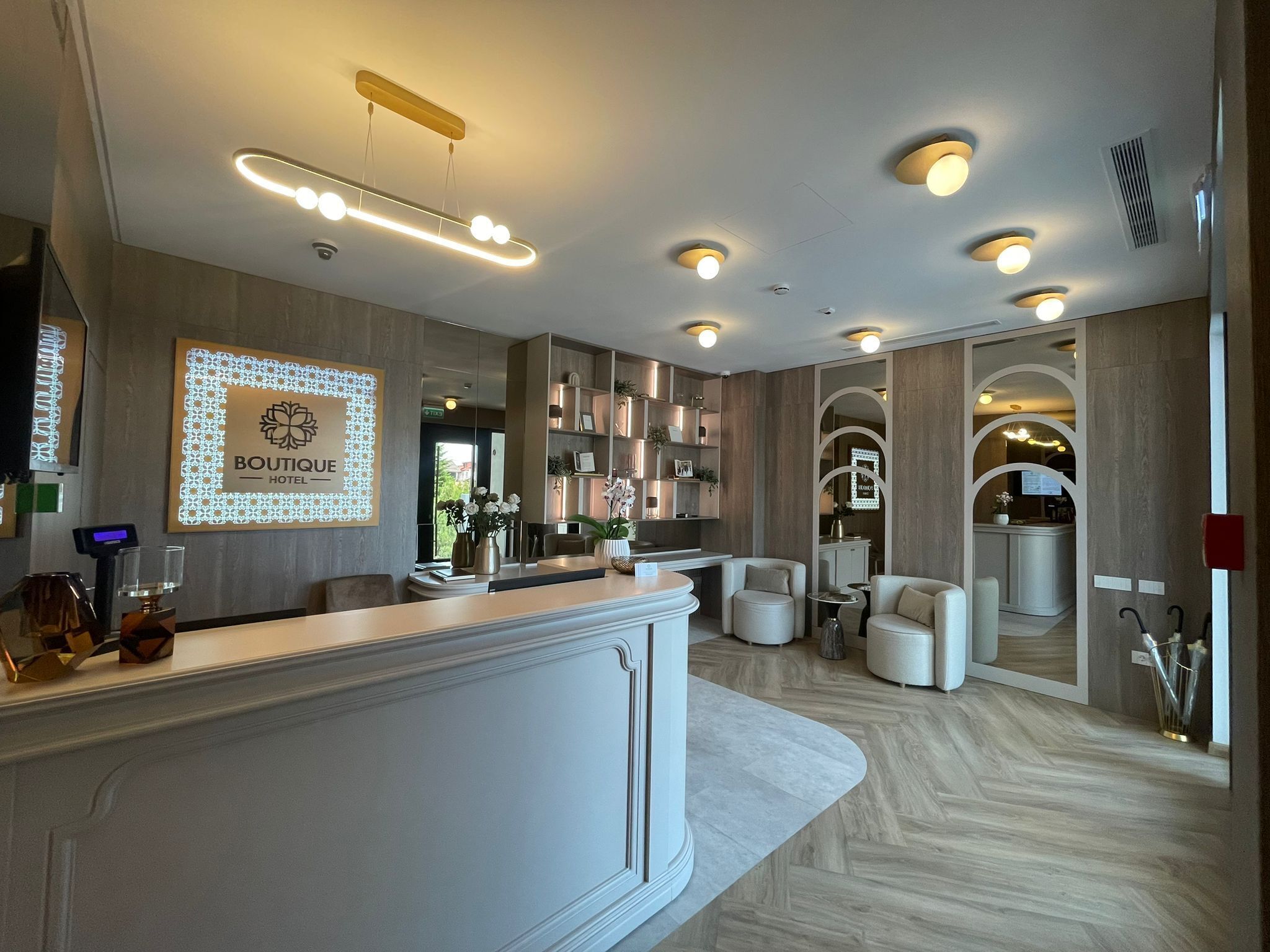 A hotel reception area with a modern design, featuring a reception desk, seating area, and a visible kitchen in the background.