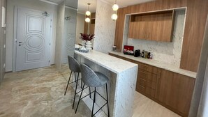 Eine moderne Küche mit Marmorarbeitsplatte, zwei Barhocker, Holzschränken und Pendelleuchten.