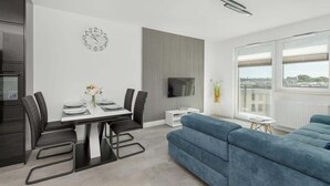 Un salon moderne comprenant un coin repas, un téléviseur à écran plat fixé au mur et de grandes fenêtres offrant une vue sur la ville.