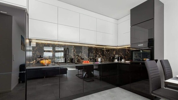 Une cuisine moderne avec des meubles de couleur noire, un pare-feu en marbre et un four encastré.