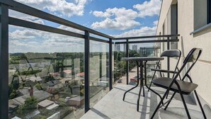 Un balcon doté d’une paroi vitrée, d’une table et de deux chaises, donnant sur un quartier résidentiel avec des maisons et un ciel dégagé.