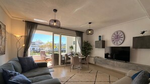 A modern living room with a sofa, a dining area, and a TV. - Golf Resort - Apartment - Sleeps4 - Pool - Parking (Torre-Pacheco)