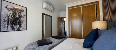 A bedroom with a bed, a ceiling fan, a radiator, a mirror, and a door.