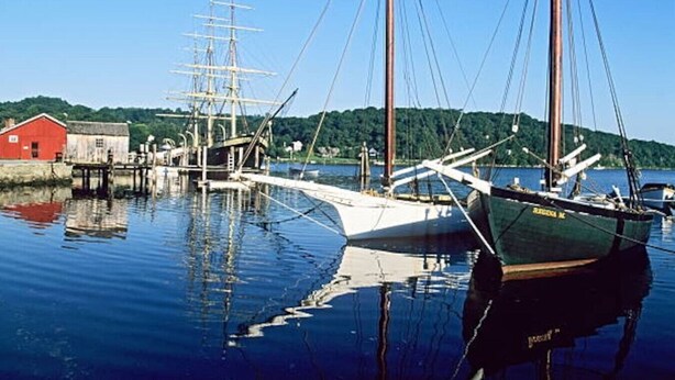 Ein traditionelles Segelschiff liegt im Hafen, in der Nähe befindet sich ein rotes Gebäude.