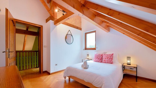 A bedroom with a wooden ceiling, a bed with white bedding, a bedside table with a lamp, and a window. - At Au Pif: family, hiking, spa bath & nature (Volmunster)
