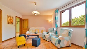 A cozy living room with a sofa, armchairs, a coffee table, and a yellow chair. There is a window with curtains, a door, and a ceiling light. - At Au Pif: family, hiking, spa bath & nature (Volmunster)