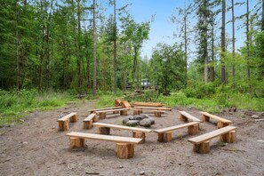 A forest clearing with a circular arrangement of wooden benches and a central fire pit.