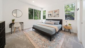 Ein modernes Schlafzimmer mit einem Bett, einem Schreibtisch, einem Spiegel und großen Fenstern.