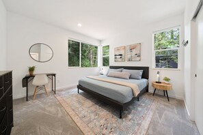Une chambre à coucher avec un lit, un bureau, une chaise, un miroir rond et des œuvres d’art accrochées au mur.