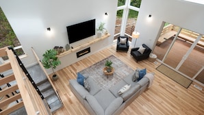 Ein modernes Wohnzimmer mit einem großen Flachbildfernseher, einem grauen Sofa und einer Holztreppe.