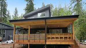 Ein modernes Haus mit einer großen Terrasse, einer überdachten Veranda und einer Treppe zum oberen Stockwerk.