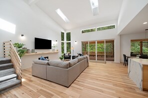 Amplia sala de estar con un sofá seccional grande, una escalera de madera y un comedor con vistas al exterior.