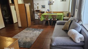 A cozy living room with a sofa, a dining table with chairs, and a kitchen area visible through an open door. - Etwas Älter Aber Fein (Villnöss)
