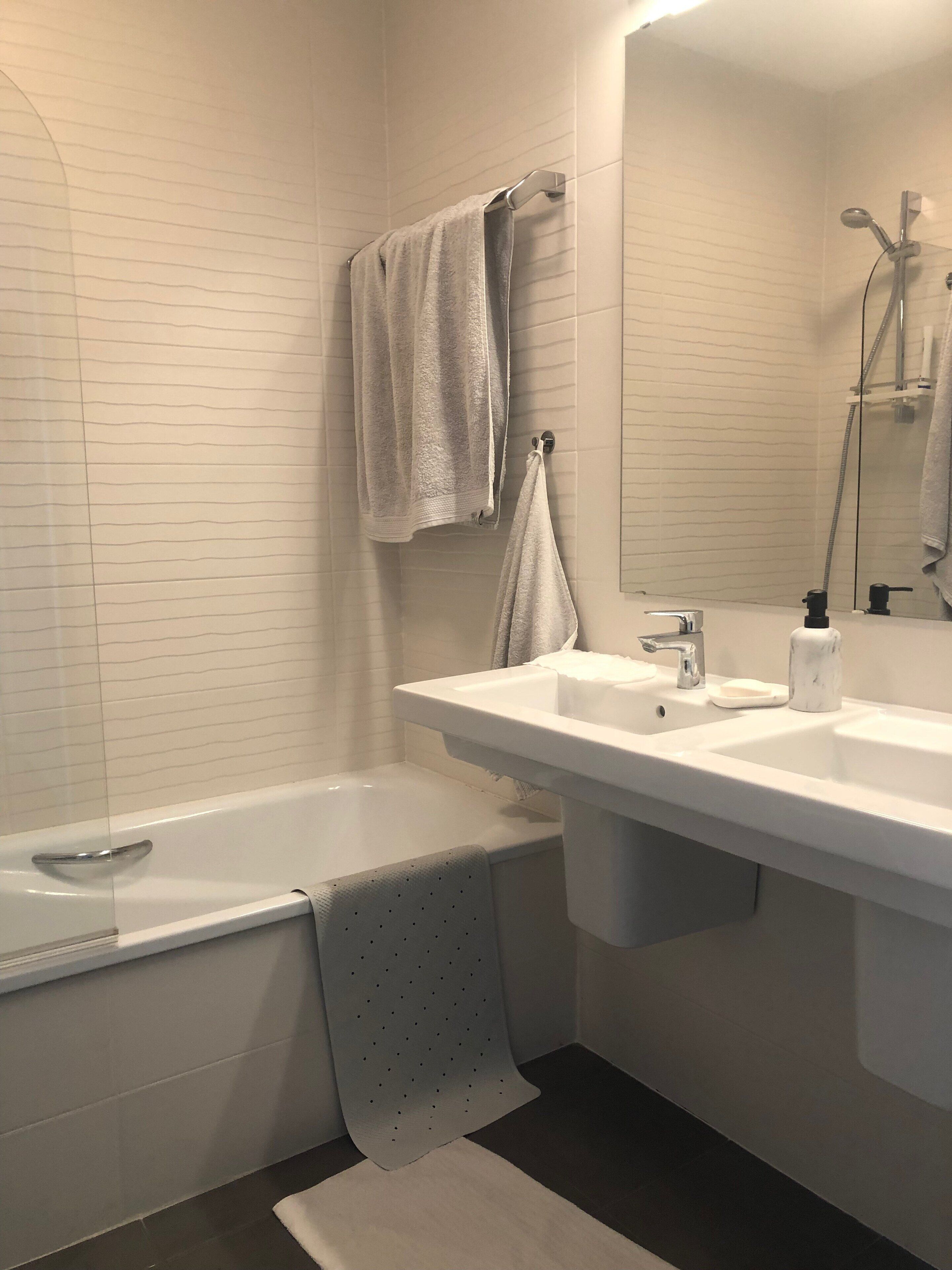 A modern bathroom with a bathtub, two sinks, and a shower.