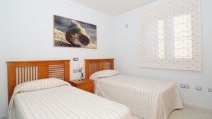 A bedroom with two beds, a nightstand, a lamp, and a large window with blinds. - Immaculate 2-bed Apartment No 5 in Playa Blanca (Yaiza)