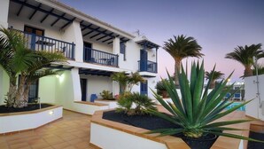 A two-story building with a balcony, surrounded by palm trees and a swimming pool. - Immaculate 2-bed Apartment No 5 in Playa Blanca (Yaiza)