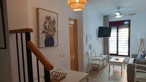 A living room with a white sofa, a TV, a table with a basket, a painting, and a staircase. - Amazing & Renovated 2-bedroom Flat in Fuengirola (Fuengirola)