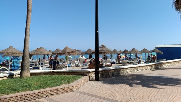 A beachside area with thatched umbrellas, lounge chairs, and a clear blue sky. - Amazing & Renovated 2-bedroom Flat in Fuengirola (Fuengirola)