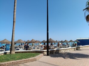 A beachside area with thatched umbrellas, lounge chairs, and a clear blue sky. - Amazing & Renovated 2-bedroom Flat in Fuengirola (Fuengirola)