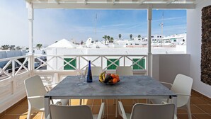Un balcón con una mesa, sillas y vistas a edificios blancos y palmeras.
