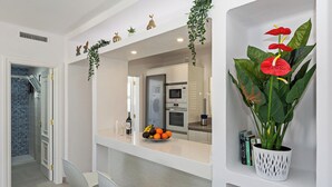 Una cocina moderna con armarios blancos, horno integrado y encimera con un bol de fruta y copas de vino.