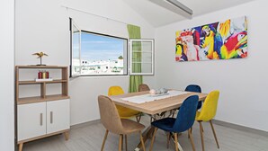 Un comedor con una mesa de madera, sillas coloridas, un armario blanco y vistas de edificios a través de una ventana.