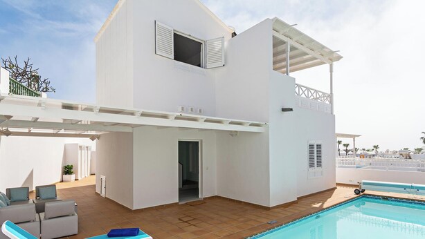 Un edificio de dos plantas con piscina, mobiliario exterior y un patio cubierto.